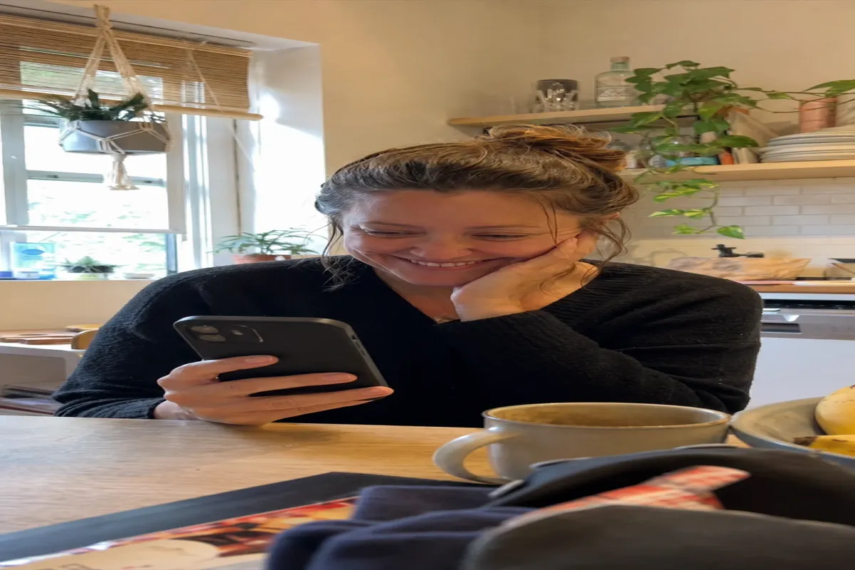 Woman relaxing at her kitchen table, smiling as she checks her phone